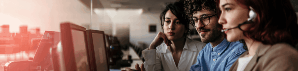 3 IT technicians looking at their desktop computers. They are wearing headsets